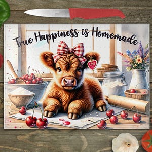 Pode incluir: Uma tábua de cortar de vidro com um bezerro Highland marrom e branco com um laço xadrez vermelho e branco. O bezerro está deitado em uma superfície branca com cerejas e farinha. O texto "True Happiness is Homemade" está escrito em preto na tábua.
