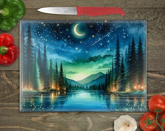 May include: A glass cutting board with a blue and green watercolor painting of a forest scene at night. The painting features a crescent moon, stars, and a lake reflecting the night sky.
