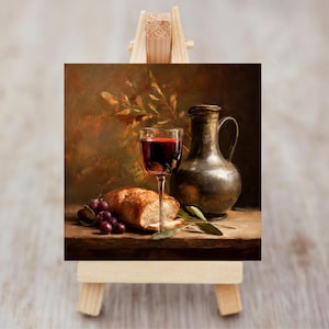 May include: A still life painting depicting a glass of red wine, a loaf of bread, and a bunch of grapes. A metallic jug is positioned next to the glass. The painting is on a small wooden easel.