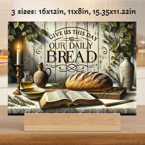 Könnte beinhalten: Ein Schneidebrett aus Holz mit einem Gemälde eines Laibes Brot, einer Bibel und einer Kerze. Das Gemälde trägt den Text "Gib uns heute unser tägliches Brot".