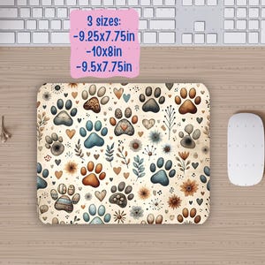 Op de afbeelding: Een muismat met een beige achtergrond en een herhalend patroon van bruine, blauwe en grijze poot afdrukken, harten en bloemmotieven. De tekst "3 maten: -9.25x7.75in -10x8in -9.5x7.75in" is in roze op een witte achtergrond gedrukt aan de bovenkant van de muismat.