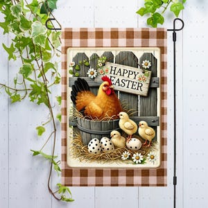Puede incluir: Una bandera de jardín decorativa con un tema de Pascua. La bandera muestra una gallina en un cubo de madera, pollitos y huevos moteados. Las palabras "Happy Easter" están en un letrero de madera, todo enmarcado por un borde a cuadros marrón y blanco.