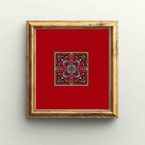 Puede incluir: Una obra de arte enmarcada con un marco dorado. La obra presenta un diseño geométrico colorido y detallado sobre un fondo rojo. El diseño incluye elementos azules, verdes, rojos y negros, creando un patrón simétrico. El marco es rectangular.