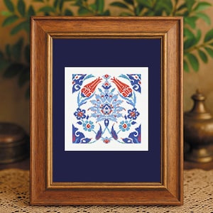 May include: A framed cross-stitch artwork featuring a symmetrical floral design in red, blue, and white. The artwork is displayed in a wooden frame with a dark blue mat. The design includes stylized flowers and leaves.