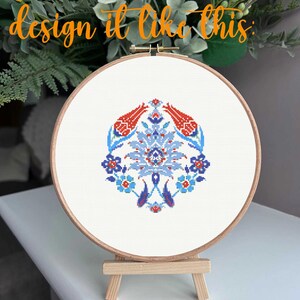 May include: A cross-stitch embroidery hoop featuring a floral design in red, blue, and white. The design is centered on a white fabric, held within a wooden hoop. The text "You can also design it like this" is in orange script.