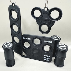 Könnte beinhalten: Ein Set aus schwarzen Plastik-Fidget-Spielzeugen mit verschiedenen Formen und Designs. Die Spielzeuge beinhalten einen Ring mit drei Löchern, ein rechteckiges Stück mit vier Löchern und den Worten "break" und "jump" sowie zwei zylindrische Stücke mit einem Logo.