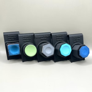 Könnte beinhalten: Fünf schwarze Halter mit dem Text "Bespoke Billiards Berlin" auf jedem. Jeder Halter hat eine andersfarbige Kreide, darunter blau, grün, grau, hellblau und dunkelblau.