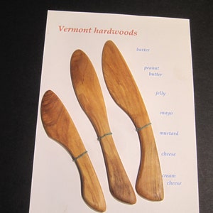 May include: Three wooden butter knives with a natural wood finish. The knives are labelled with different uses, including butter, peanut butter, jelly, mayo, mustard, cheese, and cream cheese. The text "Vermont hardwoods" is at the top of the card and "Fairfield Farm Bowls toby@fairfieldfarmbowls.com" is at the bottom.