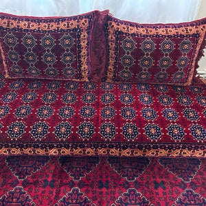 May include: A set of burgundy-colored cushions and a matching rug. The cushions have a floral pattern with gold and navy blue accents, and fringe trim. The rug features a similar design, creating a cohesive look for home decor.