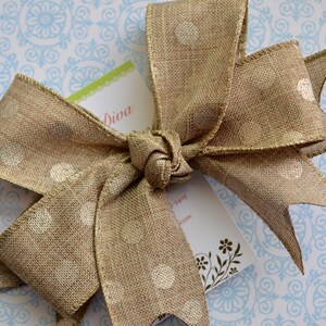 May include: A brown burlap ribbon with white polka dots tied into a bow. The ribbon is on a blue and white patterned background.
