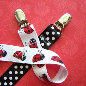 May include: Two white and black ribbon clips with silver clasps. One ribbon has a black and white polka dot pattern and the other has a white background with red ladybugs.