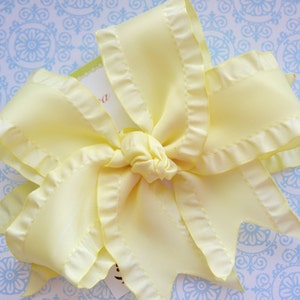 May include: A large, yellow, ruffled bow made of satin ribbon. The bow is tied in a knot in the center and has a slightly textured surface.