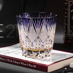 May include: A heavy-bottomed crystal tumbler featuring a deep blue upper section that transitions into a clear base. The glass is adorned with intricate geometric diamond and fan-shaped cuts, creating a textured, multifaceted surface throughout.