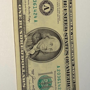 May include: A United States one hundred dollar bill. The bill features a portrait of Benjamin Franklin and the text "THE UNITED STATES OF AMERICA". The bill is green and black.