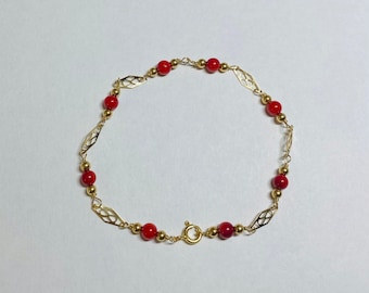 Puede incluir: Un brazalete de oro con cuentas rojas y un diseño delicado e intrincado. El brazalete tiene un cierre de broche.