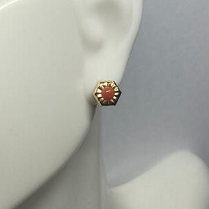 May include: A single gold stud earring with a hexagonal shape and a coral-colored center. The earring is set against a white background, showcasing its design and color.