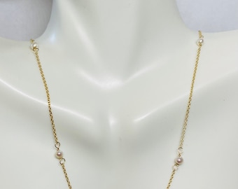 Puede incluir: Un collar de cadena dorada con cinco pequeñas perlas blancas. El collar está en un maniquí blanco.
