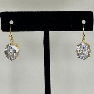May include: A pair of gold earrings with large, clear, round, faceted stones. The stones are set in a gold bezel setting and the earrings have a simple, elegant design.