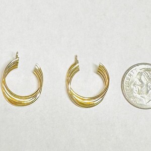 May include: Two gold-colored hoop earrings with a twisted design, next to a dime coin for size comparison. The earrings have a polished finish and a classic, elegant style. The earrings are likely made of metal.