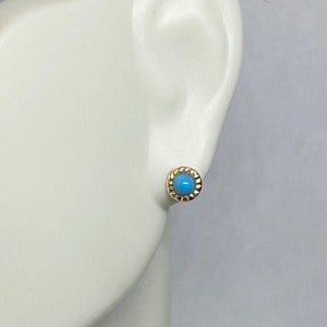 May include: A pair of gold stud earrings with a blue turquoise stone in the center. The earrings have a scalloped edge.