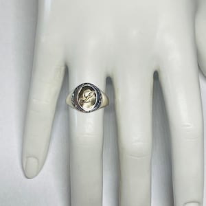 以下が含まれることがあります： 筆記体で「L」の文字が刻まれた、ゴールドの楕円形のセッティングが施されたシルバーリングです。