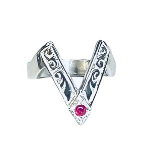 May include: A silver ring with a V-shaped design and a small red gemstone in the center.