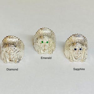May include: Three silver rings with a Native American headdress design. Each ring has a different colored gemstone in the eyes: green, blue, and clear.