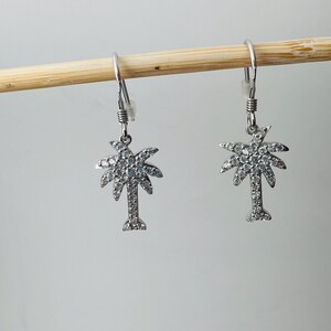May include: A pair of silver palm tree earrings with clear crystal accents.