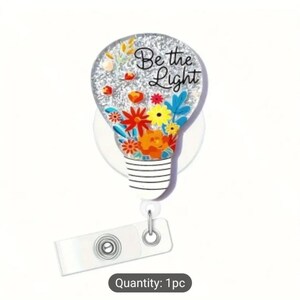May include: A silver glitter light bulb with colorful flowers and the text "Be the Light" on a white retractable badge reel with a clear plastic badge holder.