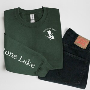 May include: A dark green sweatshirt with the text "Redstone Lake" and a white outline of a lake on the right side of the chest. The text "Redstone Lake" is also printed on the left sleeve.