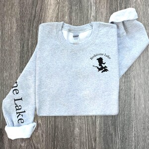 May include: A gray sweatshirt with the text "Redstone Lake" and a black outline of a lake on the front. The left sleeve has the text "Stone Lake" printed on it.