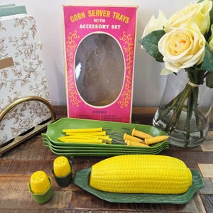 May include: A vintage corn server set with accessory set box. The set includes green corn-shaped trays, yellow corn holders, and salt and pepper shakers. The box is pink with gold accents and the text "Corn Server Trays with Accessory Set".