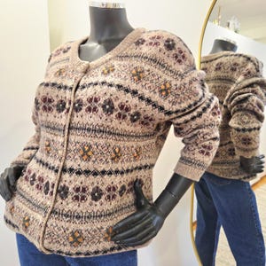 May include: A beige cardigan sweater with a floral pattern in shades of burgundy, black, and orange. The sweater has a round neckline and long sleeves. The garment is displayed on a mannequin.