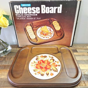 Peut inclure: Un plateau à fromage de luxe vintage en bois dur massif avec un carreau "Valencia" de 15 cm. Le plateau est de forme rectangulaire avec des compartiments pour les crackers et une tuile centrale avec un motif floral.