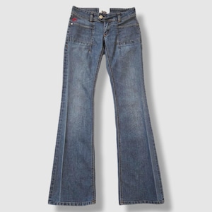 May include: Blue denim jeans with a flared leg design. The jeans feature front pockets, a button closure, and a small red logo near the left pocket. The jeans are a medium wash and have a classic five-pocket design.