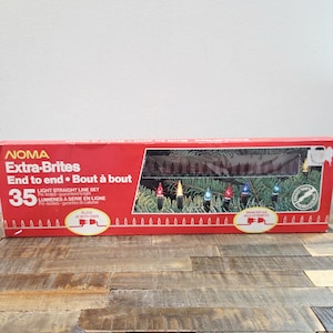 May include: A rectangular red cardboard box for NOMA Extra-Brites 35 light straight line set. The packaging features text in English and French, a clear window showing the bulbs, and an illustration of multi-coloured lights on a pine branch.