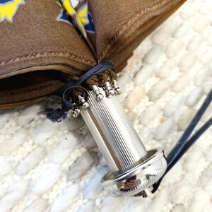 Pu&ograve; includere: Primo piano di un ombrello marrone con manico argentato. Il tessuto dell'ombrello presenta un motivo floreale giallo e blu. Il manico &egrave; scanalato e ha una base e una parte superiore decorative in argento. Un cordino blu assicura l'ombrello.