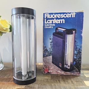 Peut inclure: Une lanterne fluorescente vintage avec un corps en plastique transparent et des accents noirs. La lanterne contient deux tubes fluorescents et est accompagnée de sa boîte d'origine, qui indique "Fluorescent Lantern Solid State Circuitry."