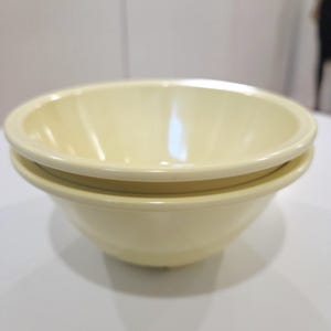 May include: Two pale yellow ceramic bowls stacked. The bowls have a simple, rounded design with a slightly flared rim. The bowls are likely for serving food. Each bowl is approximately 15 cm in diameter.