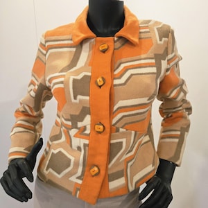 Peut inclure: Veste à motifs orange et beige avec un col et quatre boutons orange. Le motif géométrique est composé de nuances d'orange, de beige et de blanc. La veste est présentée sur un mannequin.