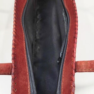 May include: Open view of a red leather handbag with a black zipper and interior. The bag has a stitched design along the edges and two small handles. The interior is lined with black fabric.
