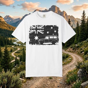 May include: White t-shirt with a distressed black graphic depicting the Australian flag and a four-wheel drive vehicle. The design includes the Union Jack, stars, and a side profile of a car. The shirt is set against a scenic mountain backdrop.