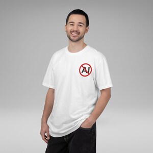 May include: White short-sleeved t-shirt featuring a red circle with a crossed-out "AI" logo. The person is wearing black jeans. The t-shirt is made of a soft material.