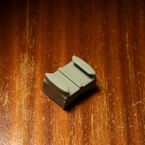 May include: A gray plastic camera mount with two prongs on the top and a curved bottom.