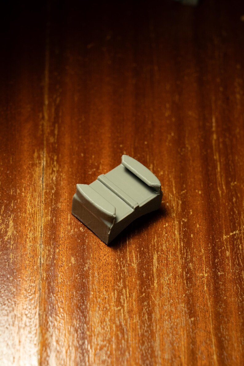 May include: A gray plastic camera mount with two prongs on the top and a curved bottom.