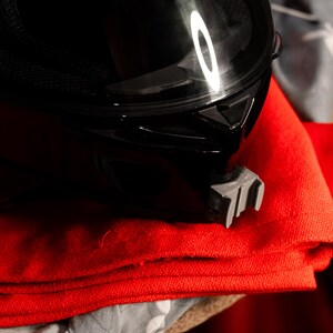 May include: A black motorcycle helmet with a clear visor sits on top of a stack of red fabric.
