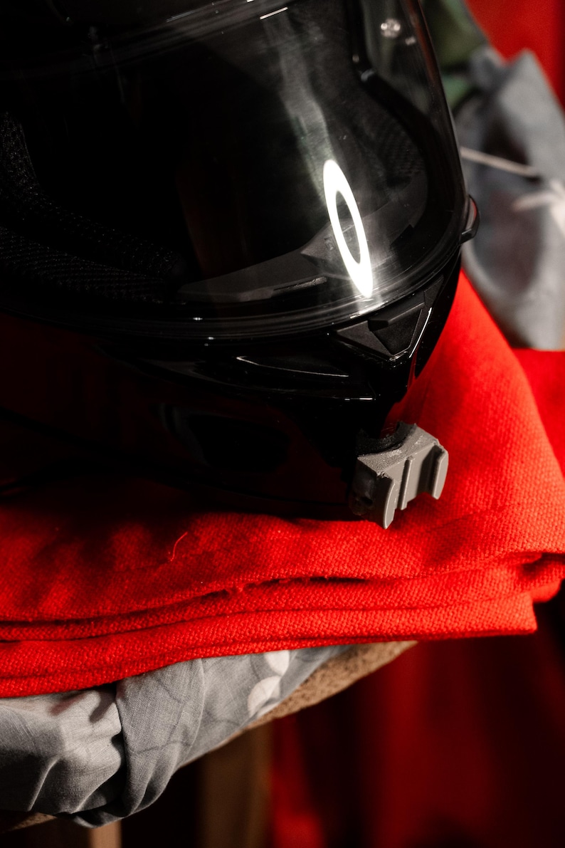 May include: A black motorcycle helmet with a clear visor sits on top of a stack of red fabric.
