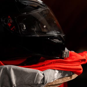 May include: A black motorcycle helmet with a clear visor sits on top of a red and gray fabric.