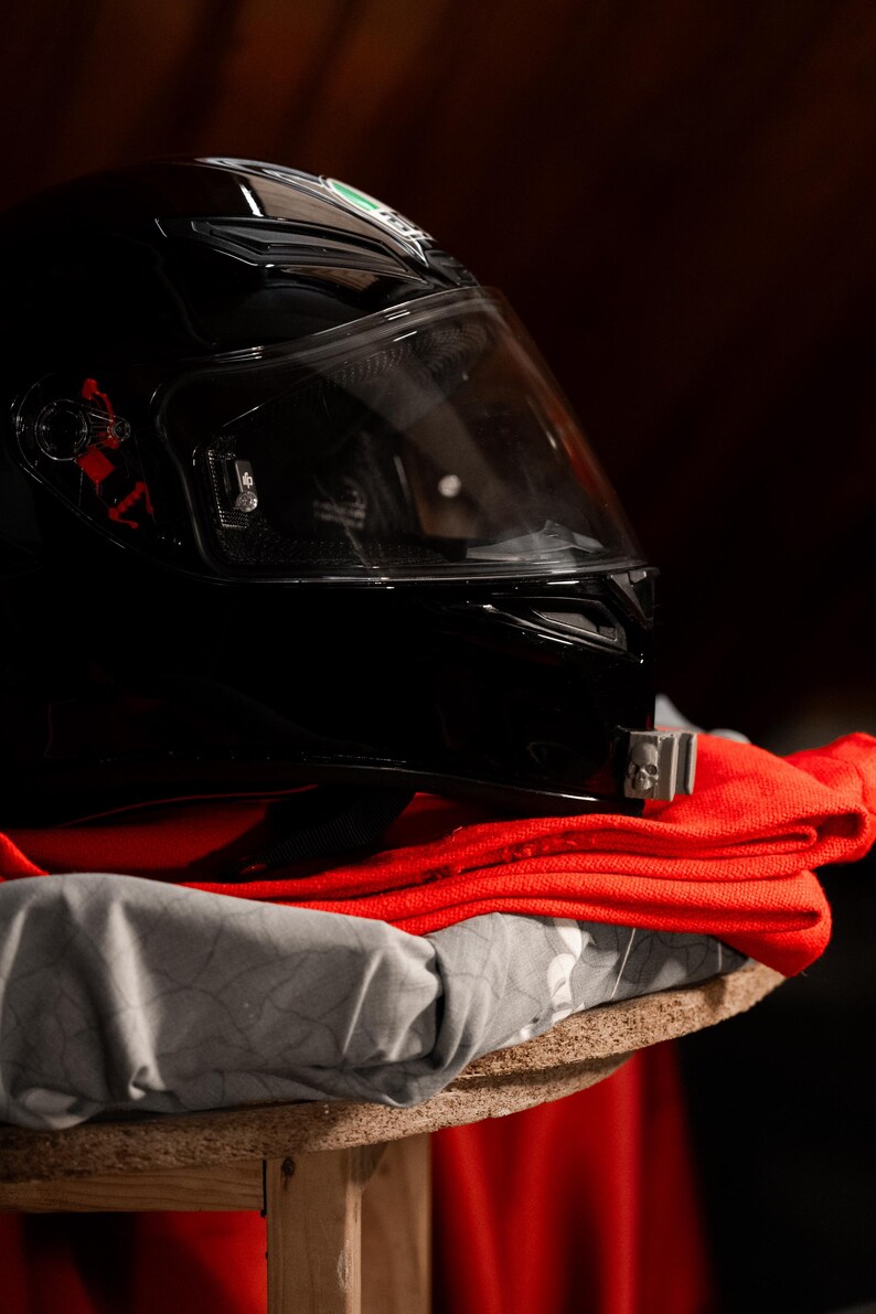 May include: A black motorcycle helmet with a clear visor sits on top of a red and gray fabric.