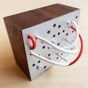 May include: A rectangular wooden block with a silver metal face. The metal face has several small holes and is wired with red and white wires. The top of the block is a dark brown wood.